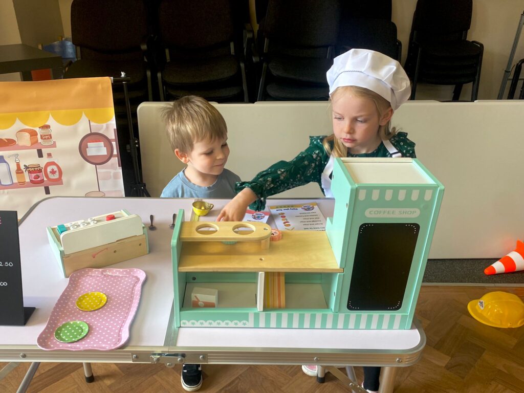Children taking part in coffee shop role play activity using a wooden café set, supporting imaginative and social play