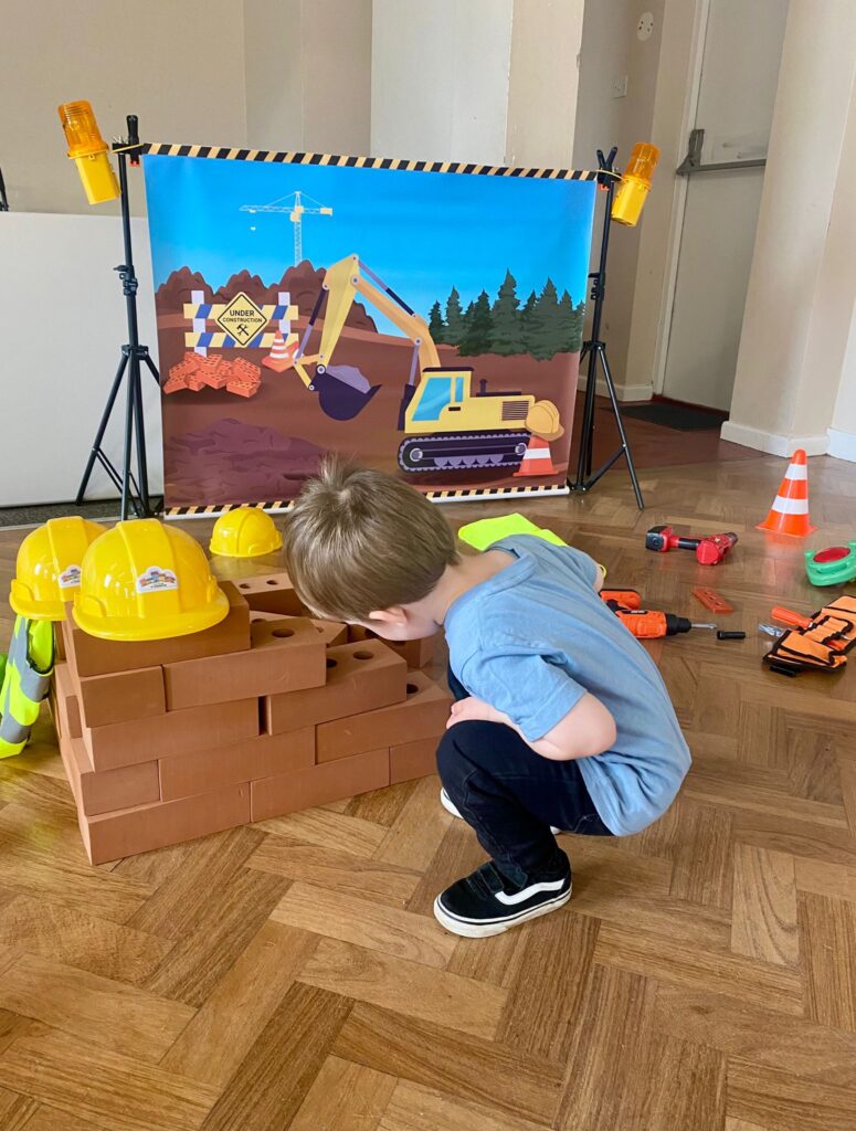 A young child engaged in imaginative construction play at The Little Village of Imagination, stacking play bricks and exploring a pretend building site role play area.