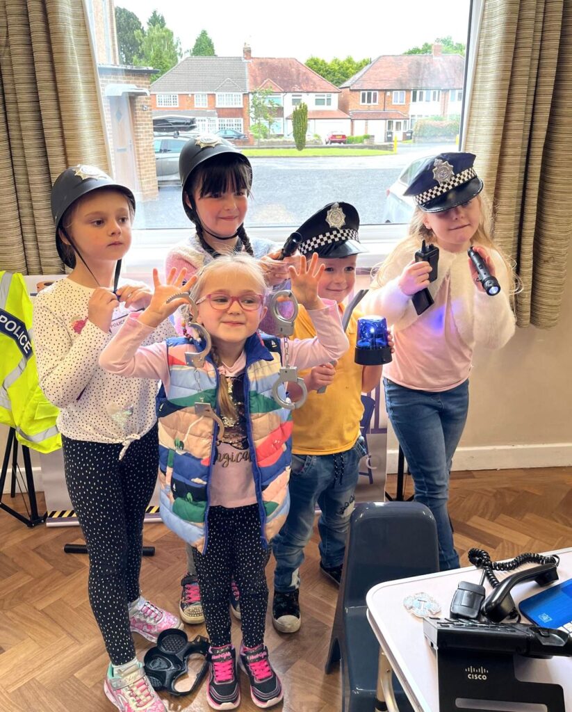 Group of children dressed as police officers during a role play session at The Little Village of Imagination, using props such as handcuffs, walkie-talkies, and helmets to explore imaginative play.