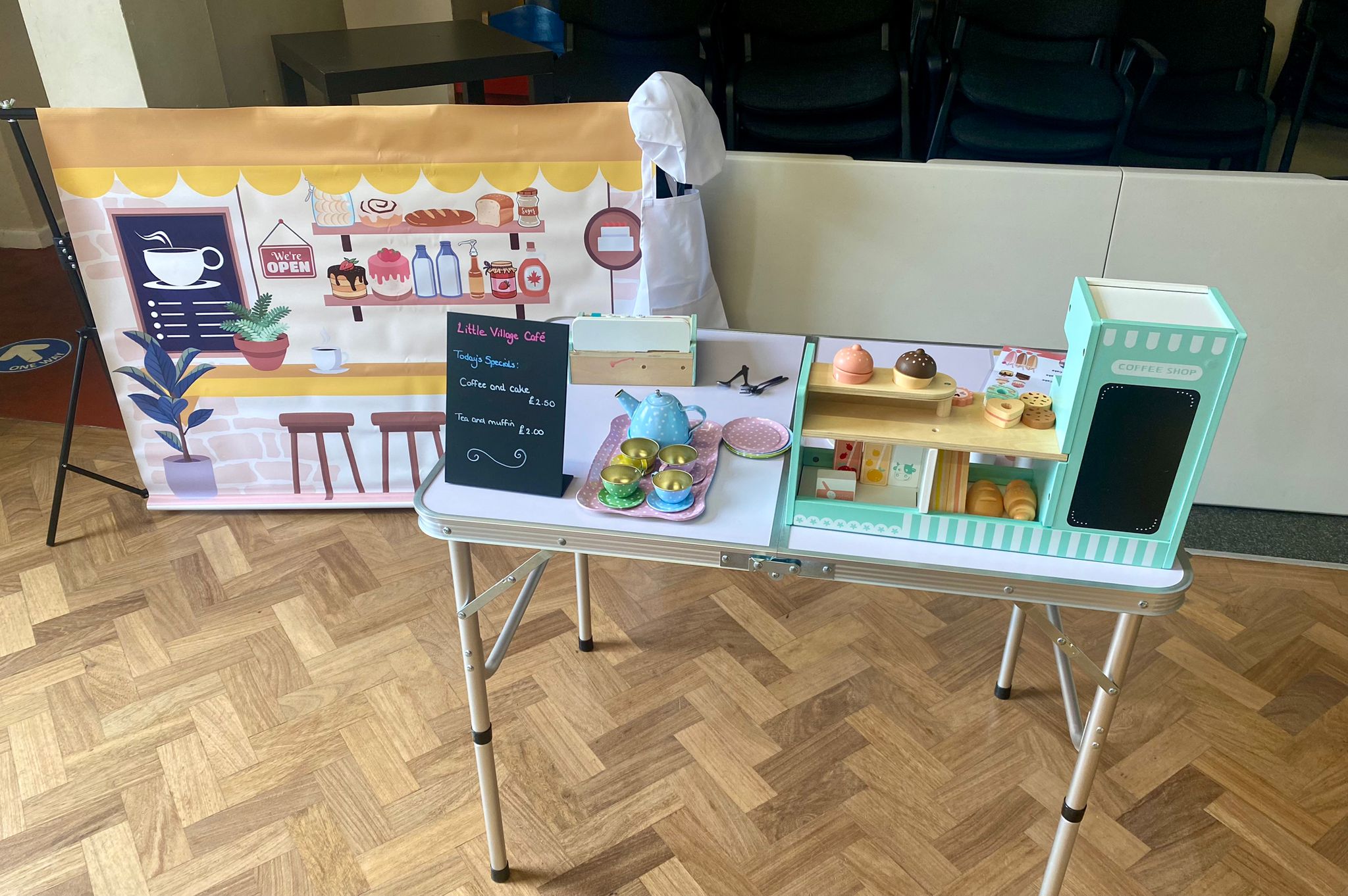 Little Village Café role play area with a play coffee shop counter, wooden cakes, a polka dot tea set and a chalkboard specials menu