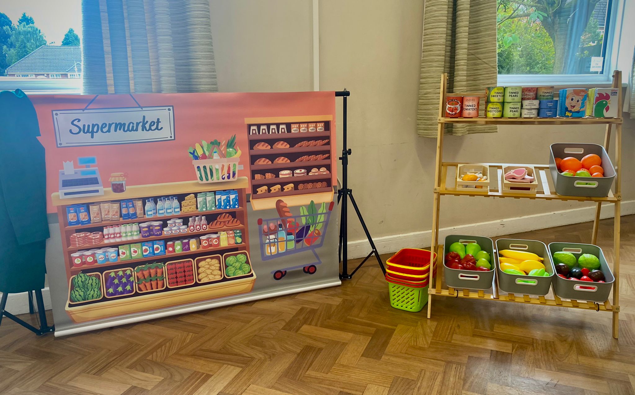 Supermarket role play area for a kids' party, with shelves of play tins and cereal boxes, baskets of play fruit and veg and shopping baskets