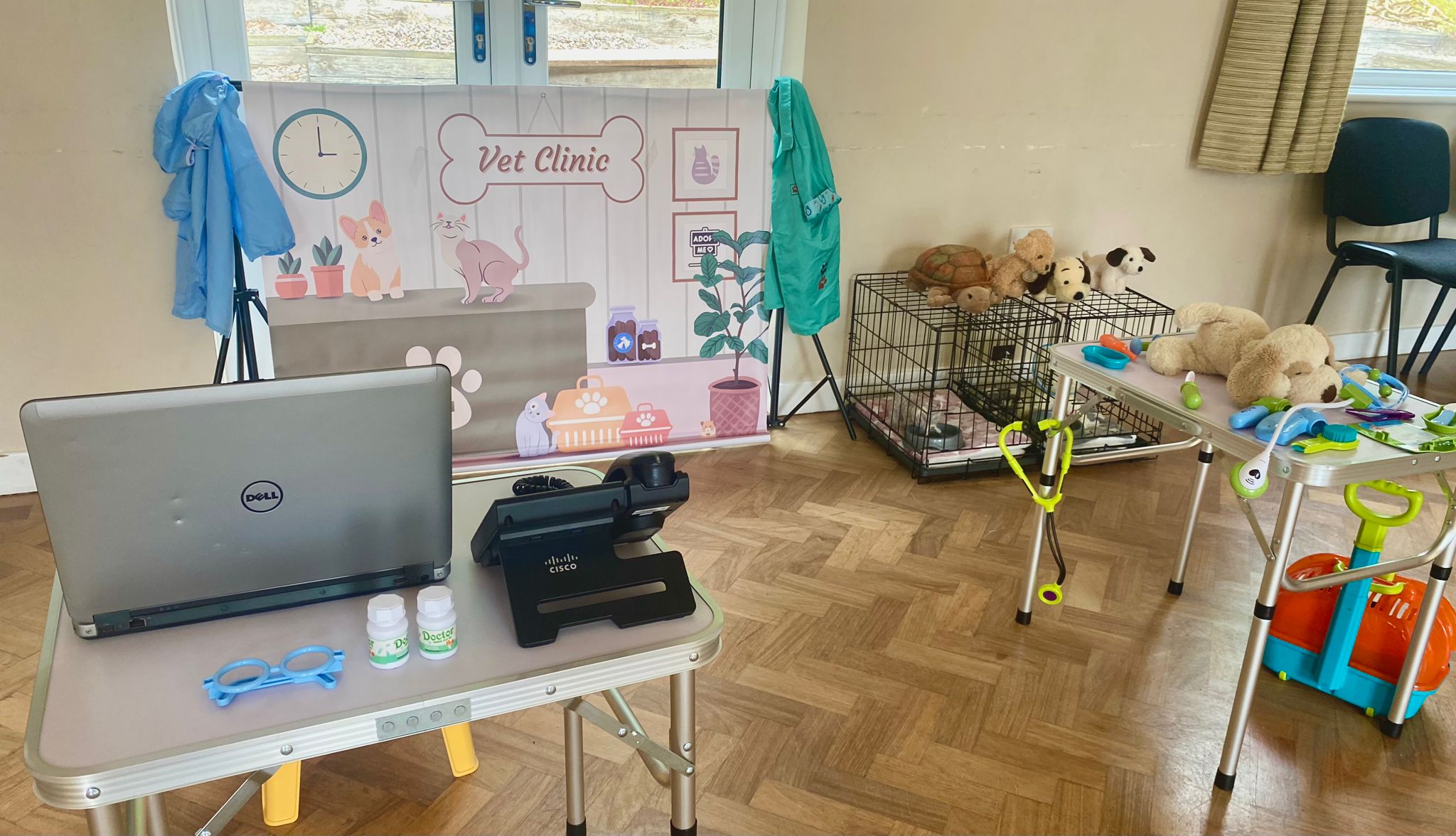 Vet clinic role play area with vet scrubs, toy medical kit, cuddly toy patients, pet crates and a reception desk with laptop and phone