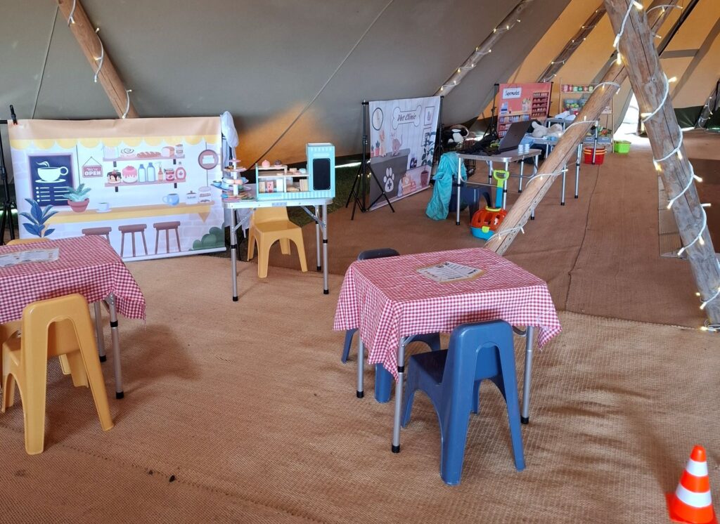 Mobile role play village set up for a children's party, with café tables, vet clinic and supermarket role play areas under fairy lights